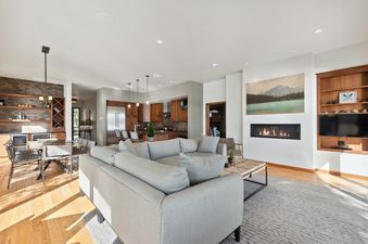 A spacious and inviting open-concept living area at The Swan Lake House, featuring a light grey sectional sofa, a modern linear fireplace, and an adjoining dining and kitchen area.