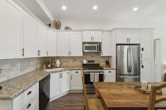 A modern kitchen in The Mason 1052 with white cabinets, granite countertops, and stainless steel appliances.