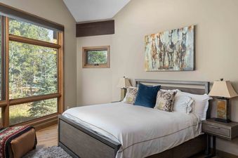 A hotel bedroom with a large bed, a window with a view of the trees, and a painting above the bed.