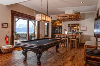 A modern basement rec room with a pool table, a bar, and a large screen television.