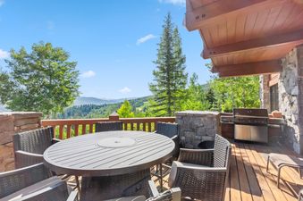 An outdoor deck with a dining table and chairs, a BBQ grill, and stunning mountain views under a clear sky at Blue Bird Vista at Hummingbird Lodge.