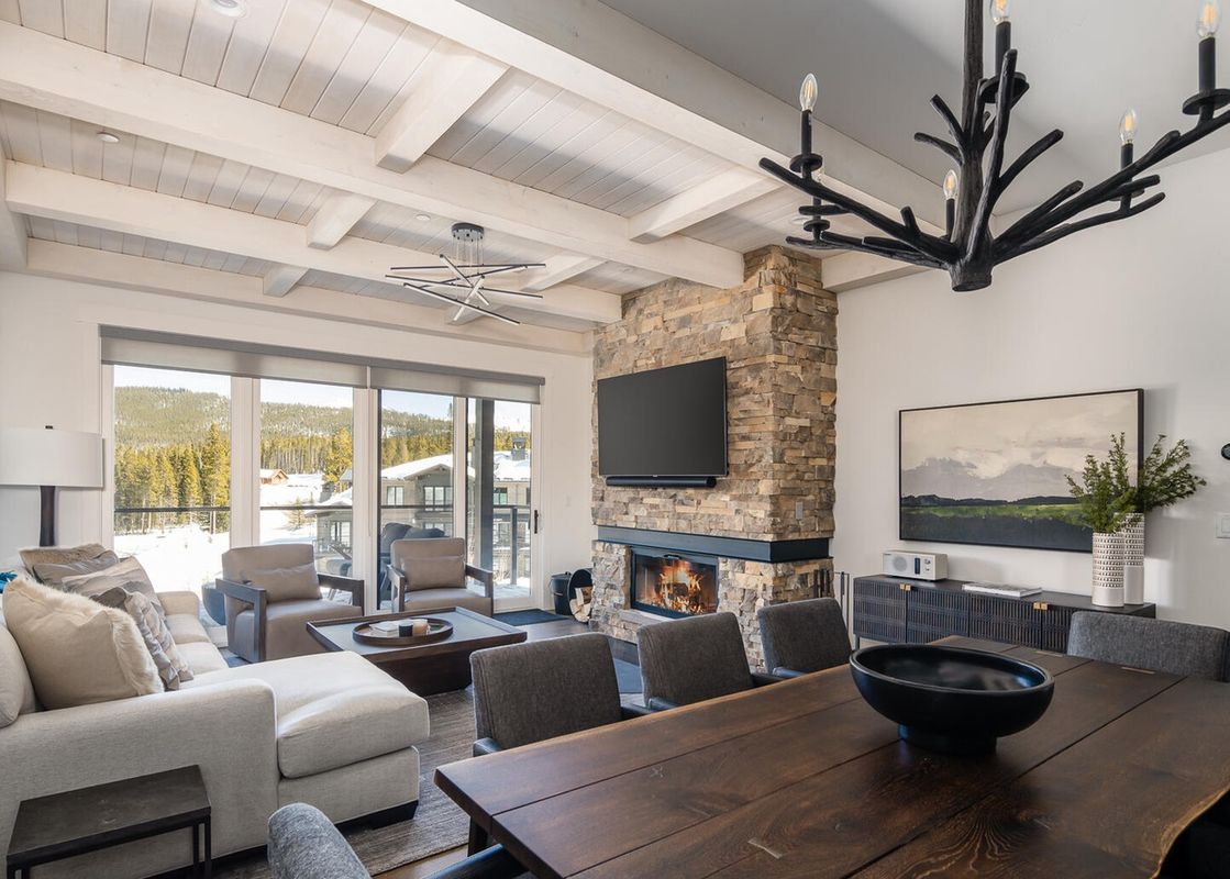 The living room of Moonlight Basin 16 Wildwood, featuring a fireplace and large windows with mountain views.