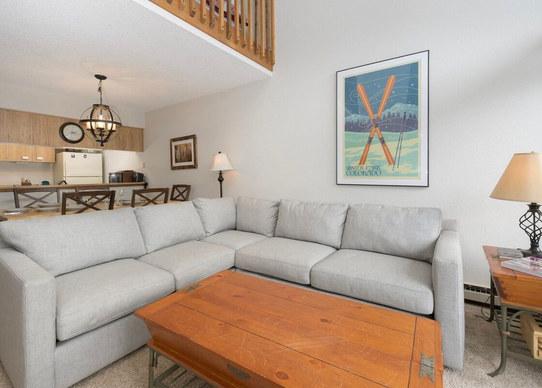 The living area of Meadow Ridge 31 features a large sectional sofa, a wooden coffee table, and a unique ski-themed wall art, with the kitchen and dining area visible in the background.
