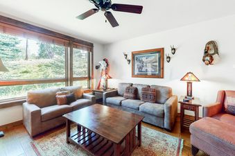 A cozy living room at BlueSky Breckenridge 205 features comfortable seating, a large window with an outdoor view, and rustic decor.