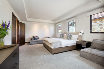 The master bedroom in Lumiere Five Bedroom Penthouse features a king-sized bed with a plush white duvet, large windows with mountain views, a wood-framed headboard, and a side table with a lamp.