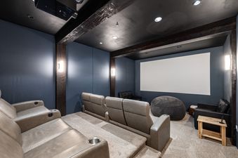 A private home theater room at Canyons Red Pine Chalet 91 featuring tiered leather reclining seats, a large projection screen, and a cozy atmosphere.