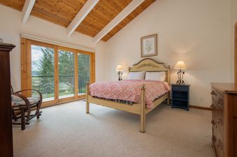 A cozy bedroom at Fisher House featuring a wooden bed, vaulted ceiling, and sliding glass doors opening to a scenic balcony.