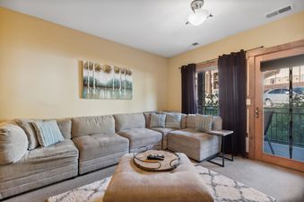 A cozy and spacious living room at Pines Unit 240, featuring a large L-shaped sectional sofa, a plush ottoman, and a sliding glass door leading to a balcony.