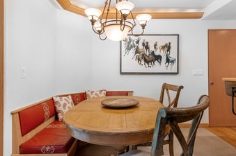 A cozy dining area featuring a wooden oval table, a built-in red upholstered bench with patterned pillows, and a large horse painting on the wall.