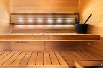 A wooden sauna interior with two benches and a bucket.