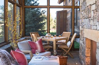A cozy outdoor patio at The Lodge at Shooting Star 01 with a dining table, seating, and a fireplace, surrounded by large windows overlooking a scenic landscape.