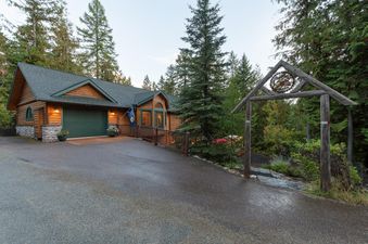 The exterior of Whispering Pines Whitefish at dusk, showcasing the inviting entrance with a rustic wooden archway and a cozy wooden house nestled among evergreen trees.