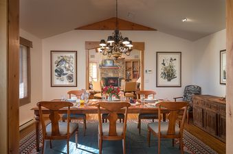 A beautifully set wooden dining table with a chandelier overhead, offering a clear view of a fireplace in the adjacent room.