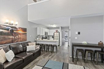 Wolf Lodge Condo 1412 offers a bright and open living space with a leather couch, a large picture on the wall, and access to the kitchen area, dining room, and hallway. The kitchen features white cabinets, a stainless steel refrigerator, and a breakfast b