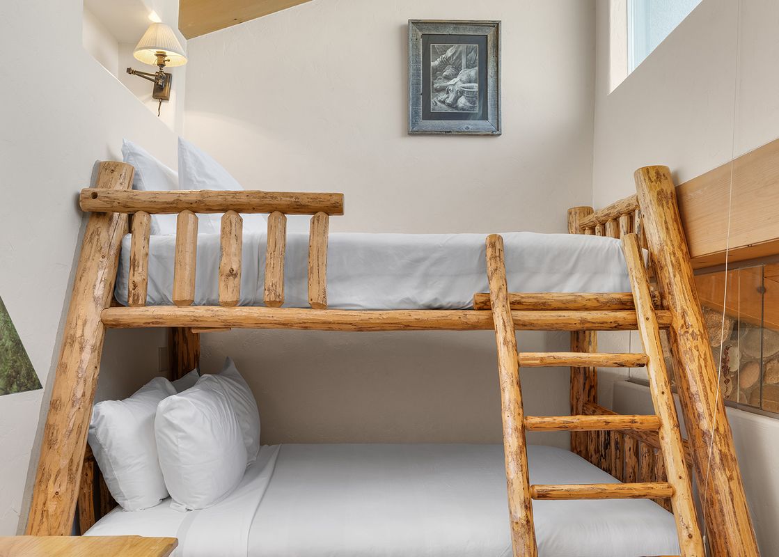 A cozy bunk room at Vantage Point 503 features rustic log bunk beds with white bedding, a decorative lamp, and a window providing natural light.