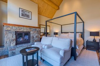 A cozy bedroom in See Forever Residence 110 features a dark wood four-poster bed, a stone fireplace, and a comfortable seating area.