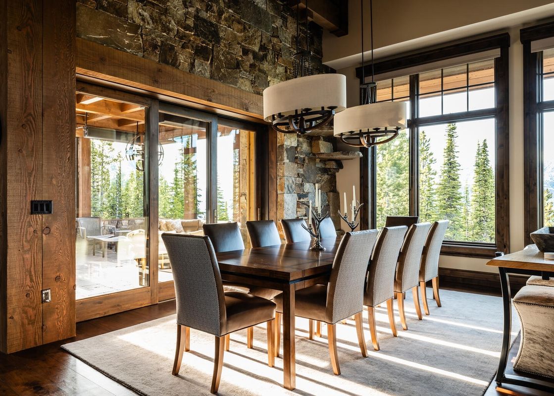 The dining room at 7 Renegade Rd Moonlight Basin Lodging has a large wooden table with six chairs, and a window with a view of the forest.