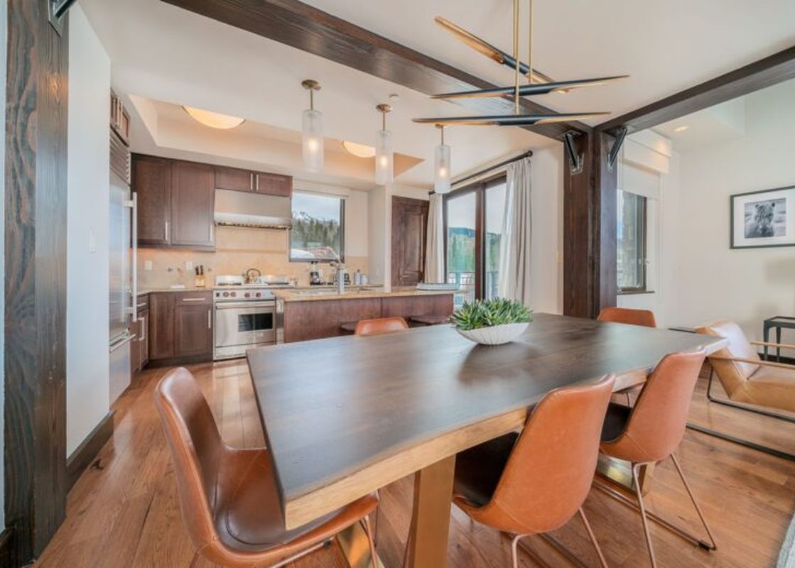 The dining area in Lumiere 2 Bedroom Suite features a large table with seating for six, modern light fixtures, and a view of the mountains.