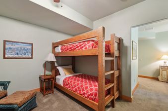 The bunk room at Northwoods Escapes features wooden bunk beds with red and white bedding, a bedside lamp, and a ski resort map on the wall.
