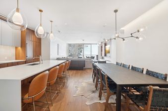 A modern open-concept living space in Founders Place 2403 featuring a kitchen island with bar stools, a long dining table, and a lounge area with views of a snowy landscape.