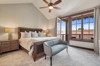 The comfortable bedroom in Silver Star 104 is adorned with neutral tones, a large bed with a dark wood frame, and a chic bench, all illuminated by a decorative table lamp.