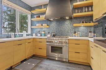 A modern kitchen with oak cabinets, a blue tiled backsplash, and stainless steel appliances.