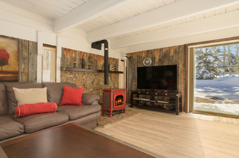 A cozy living room at 45 Idelwild features a large brown leather sectional, a red electric fireplace, and a big screen TV, with a sliding glass door leading to a snowy exterior.