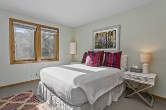 A bedroom in 2060 Solamere Drive features two windows, a white bed with colorful accent pillows, and a nightstand.