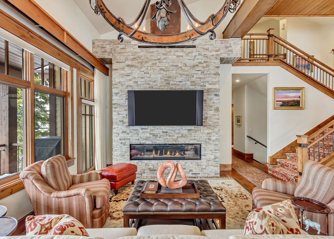 A cozy great room inside The Lookout Home featuring a large stone fireplace, plush seating, and wooden staircases.