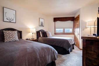 A cozy bedroom at Chateau Chamonix CX222 with two twin beds, rustic animal art, and a window offering mountain views.