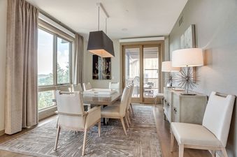 An elegant dining room with a wooden table, upholstered chairs, a stylish sideboard, and large windows looking out to nature.