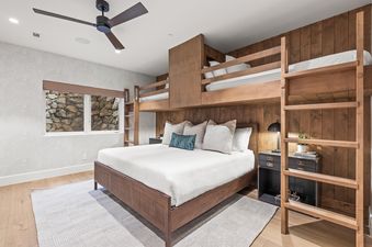 A modern rustic bedroom at Sun Ridge Vista with a queen bed, two built-in bunk beds, and a window looking out onto a stone wall.