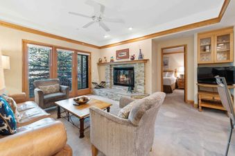 The Charter G210 living room with a lit fireplace, comfortable seating, and glass doors opening to a balcony with an exterior view of trees.