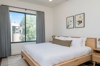 A bedroom with a king-sized bed, a nightstand, and a window with a view of trees.