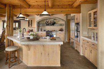 A rustic yet modern kitchen with natural wood beams, a light-toned kitchen island, and stainless steel appliances.