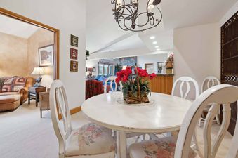 A round white dining table with floral chairs and a red tulip centerpiece, connected to a cozy living area in The Charter E430.