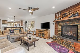 A cozy living room in Snow Flower 56 Park City with a stone fireplace, brown sofas, a wooden coffee table, and a TV on an entertainment console.