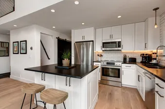 A modern kitchen with white cabinets, black countertops, and stainless steel appliances.