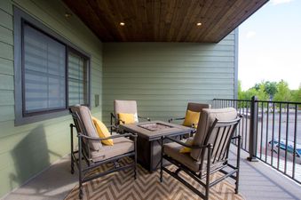 A private balcony at Baker Loft 203 with a modern fire pit, comfortable chairs with yellow pillows, and a chevron-patterned rug.