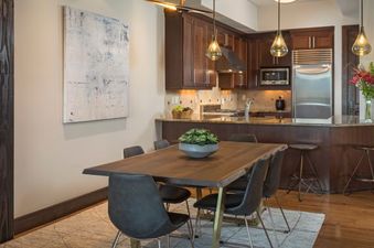 A dining table with six chairs in the Lumiere Four Bedroom Residence. The table is made of wood and has a live edge. The chairs are black leather and have gold accents.