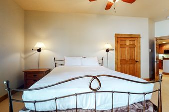 The bedroom at EagleRidge Lodge 300 features a king-size bed with a white duvet and two pillows. The room has wood floors, a ceiling fan, and a nightstand with a lamp next to the bed.