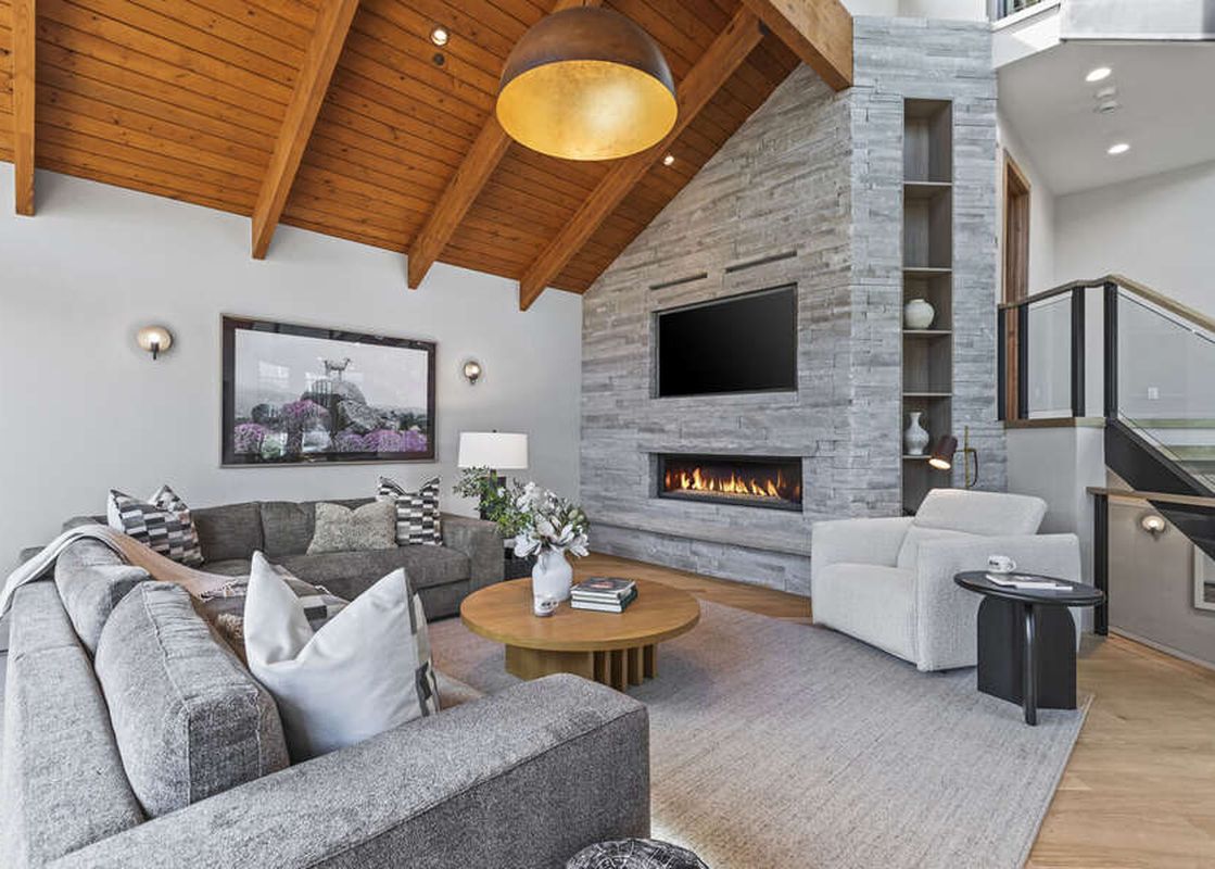 A spacious living room at Pinnacle in Deer Valley features vaulted wooden ceilings, a stone fireplace, and comfortable seating.