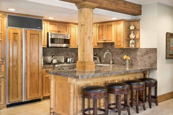 A fully equipped kitchen features custom wooden cabinetry, granite countertops, and a central island with bar seating, all illuminated by recessed lighting.