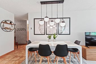 A modern dining room with a white table, black chairs, and a black light fixture hanging above.