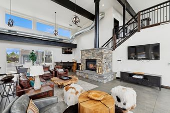 A spacious and stylish living room with a large stone fireplace, comfortable leather sofas, and modern industrial design elements.