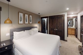 Manor Vail 165 offers a spacious bedroom with a king-size bed, a plush grey headboard, and a large window with a view of the surrounding area.