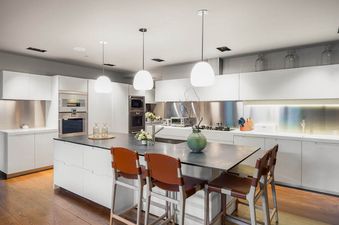 The contemporary kitchen at Riverbend House features white cabinets, stainless steel appliances, a large island with dark countertop, and brown leather bar stools.