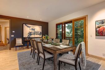 Elegant dining room at Sleeping Indian Jackson Hole with a rustic wooden table set for six and large glass doors opening to the outdoors.