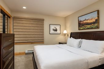 A cozy bedroom with a king-size bed, dark wood furniture, and artistic decor, perfect for relaxing after a day in the mountains.