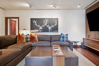 A spacious and inviting living area in Solaris PHHW, featuring a large brown sectional sofa, a coffee table with a wooden tray, and a striking deer artwork on the wall.